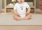 Baby wearing a white onesie with text and graphics on a beige background