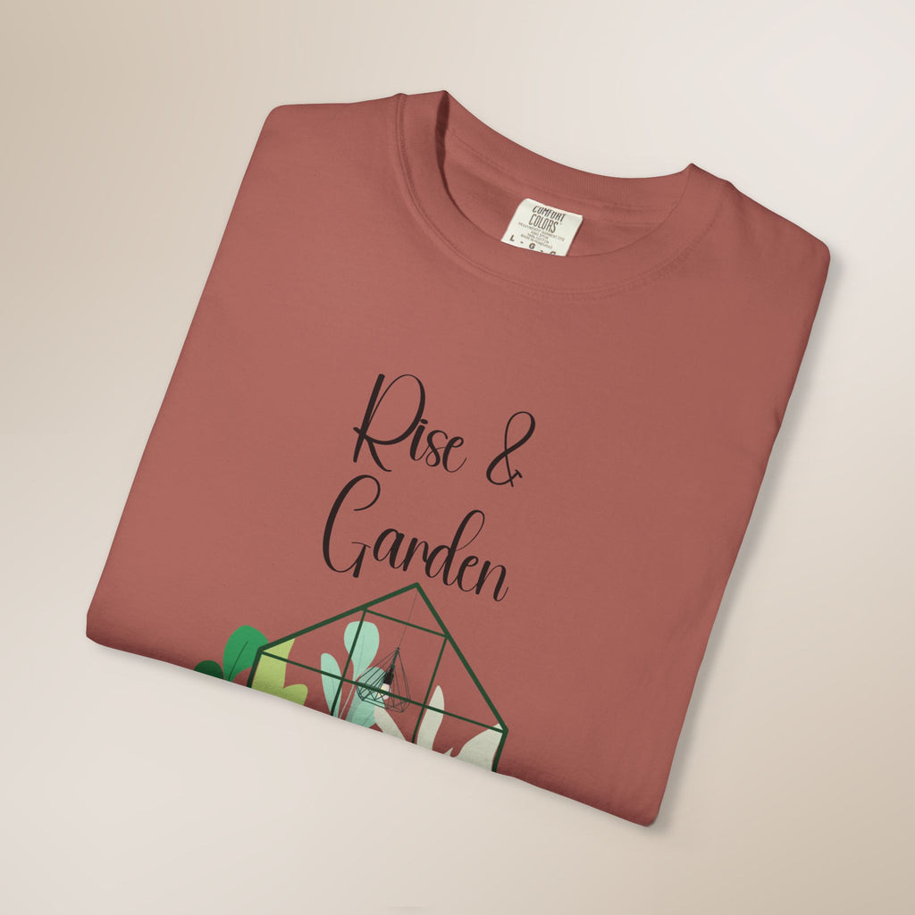 Folded terracotta-colored t-shirt with 'Rise & Garden' text and plant design on a beige background