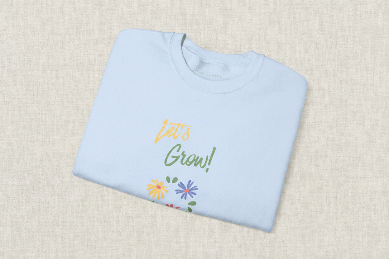 Folded light blue shirt with 'Let's Grow!' text and floral designs on a white background