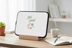 Small screen device on a wooden stand with 'Let's Grow!' text and flowers on a desk with a cup and notebook.