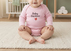 Baby wearing a pink 'Baby Gardener' onesie sitting on a carpeted floor.