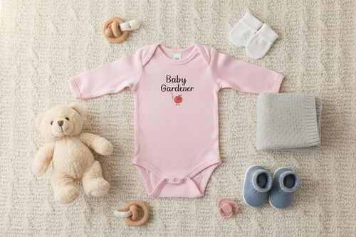 Pink baby onesie with 'Baby Gardener' text, teddy bear, socks, and booties on a beige surface
