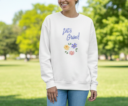 Person wearing a white sweatshirt with 'Let's Grow!' text and floral designs outdoors.