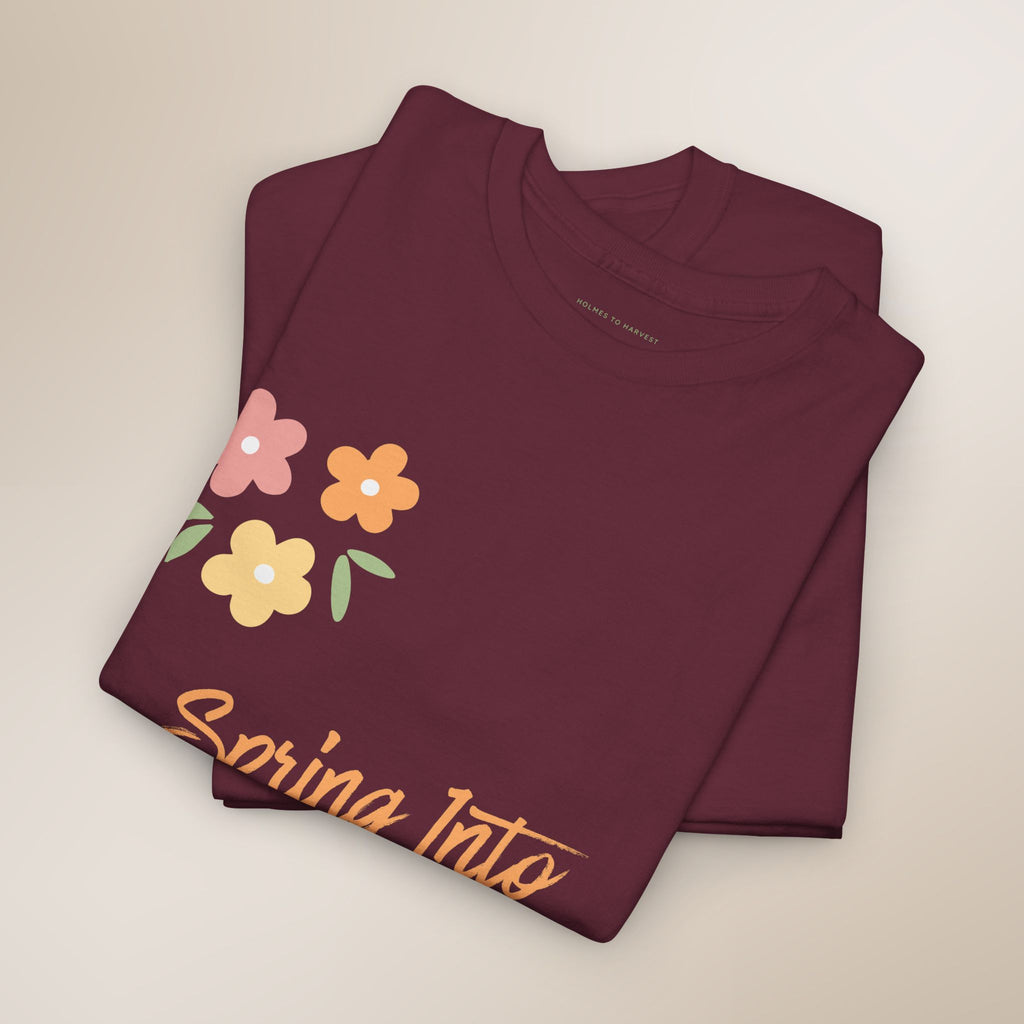 Folded maroon t-shirt with floral design and 'Spring Into' text on a beige background