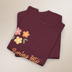 Folded maroon t-shirt with floral design and 'Spring Into' text on a beige background