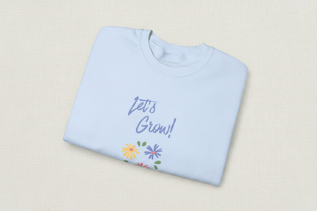 Folded light blue sweatshirt with 'Let's Grow!' text and floral designs on a white background