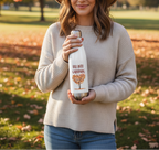 Person holding a white bottle with 'Fall into Gardening' design in an outdoor setting.