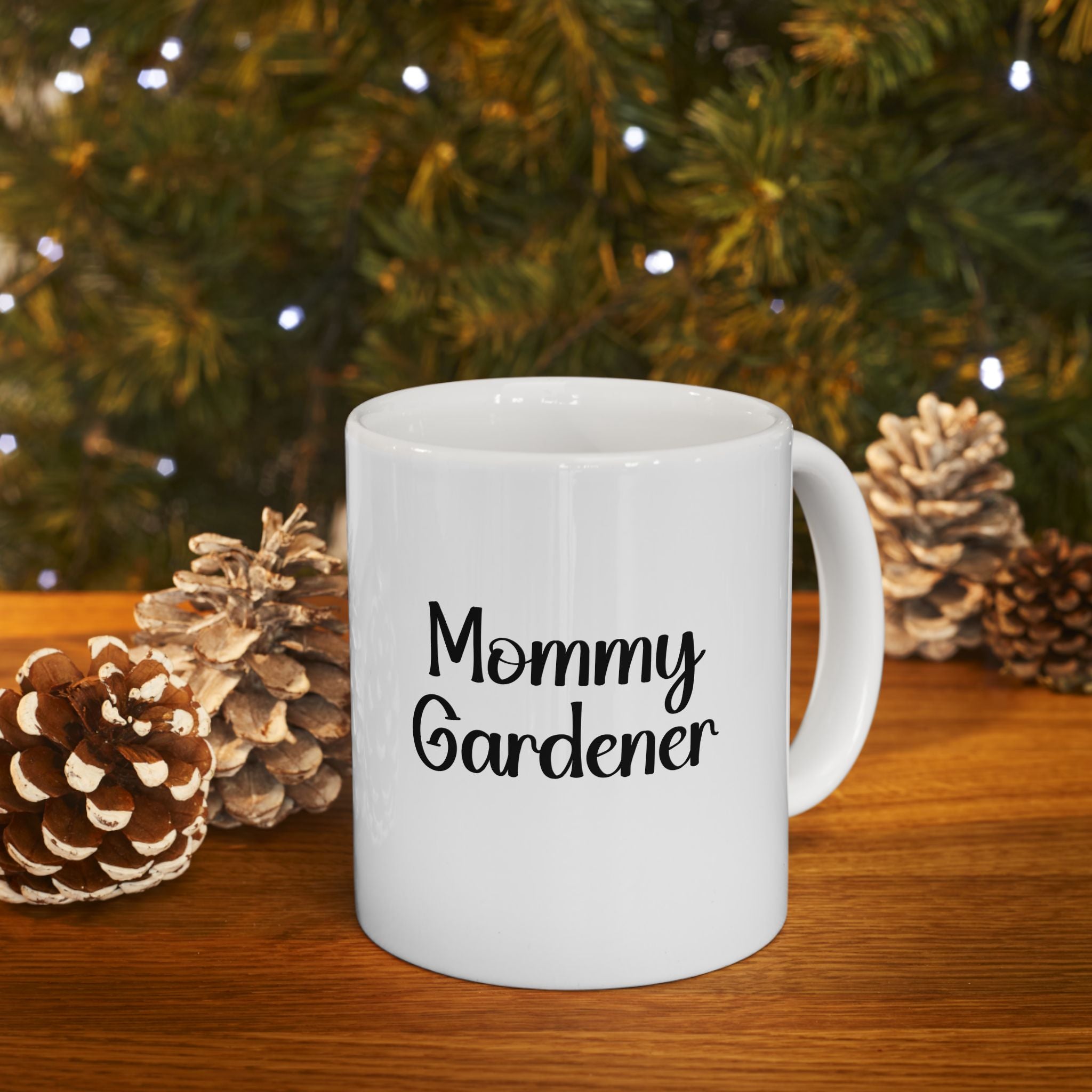 White mug with 'Mommy Gardener' text in front of a Christmas tree and pinecones.