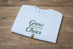 Light blue t-shirt with 'Grow a Little Cheer' text on a white background