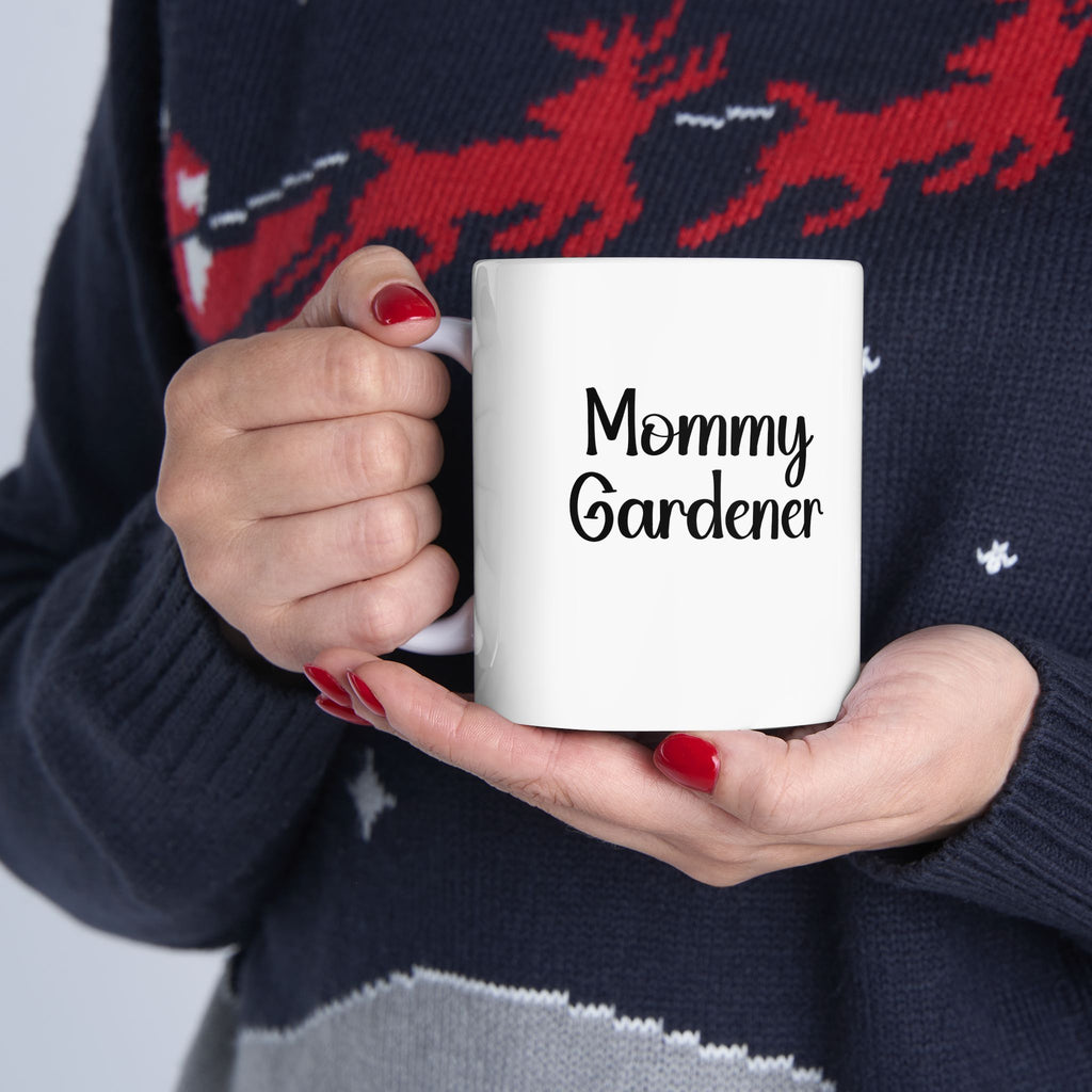 Person holding a white mug with 'Mommy Gardener' text, wearing a navy sweater with red deer design.