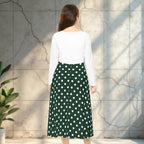 Woman wearing a white top and green polka dot skirt against a textured wall.