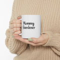 Person holding a white mug with 'Mommy Gardener' text, wearing a beige sweater.