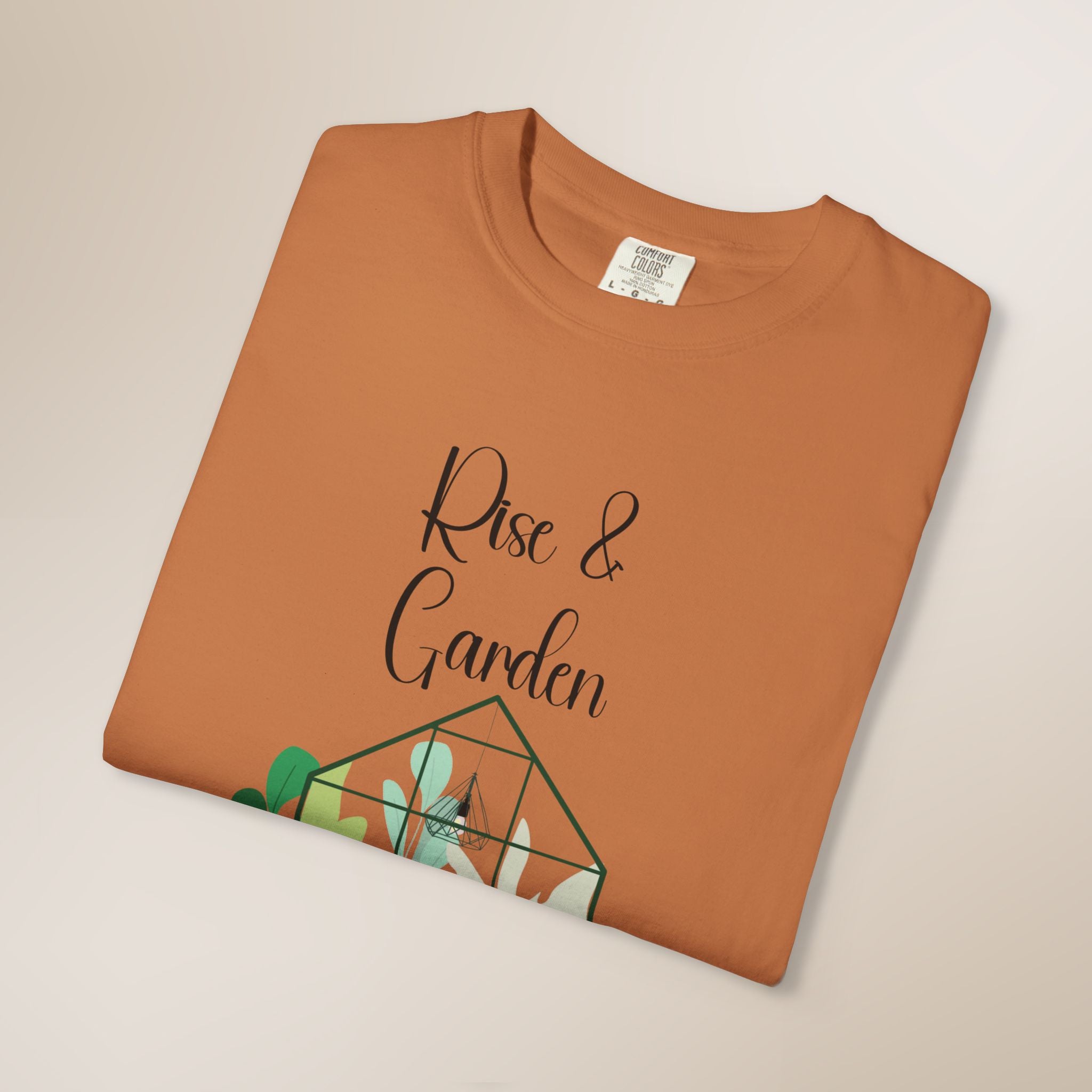Folded brown t-shirt with 'Rise & Garden' text and plant design on a beige background