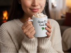 Person holding a mug with text and whipped cream, cozy indoor setting
