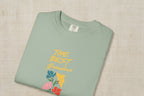 Folded green t-shirt with colorful floral design and text on a beige background