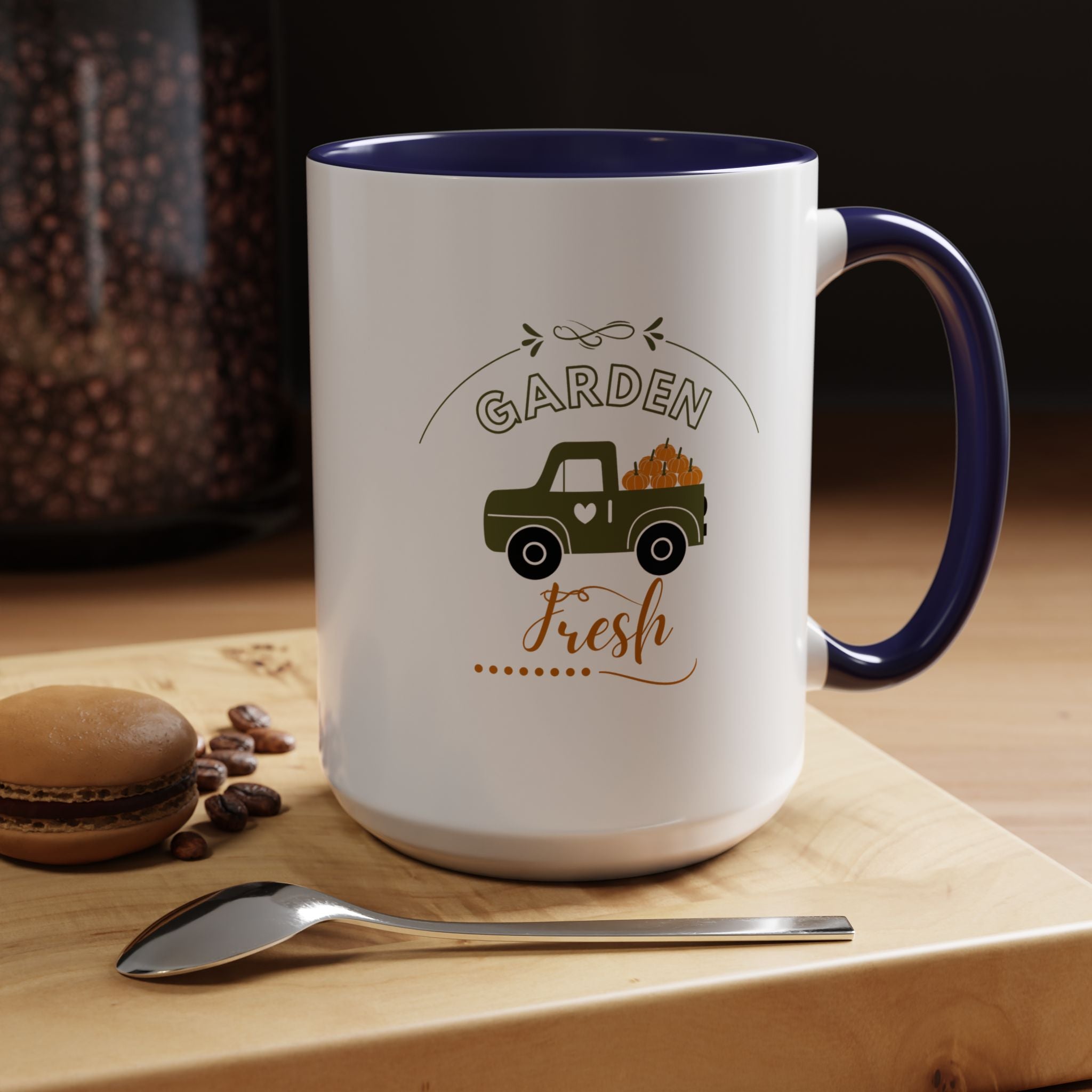 White mug with blue interior and handle, featuring a truck and 'Garden Fresh' text, on a wooden surface with coffee beans and a macaron.