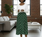 Woman wearing a white top and green polka dot skirt in a modern living room.
