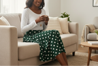 Woman sitting on a couch wearing a white long-sleeve shirt and green polka dot pants, holding a phone.