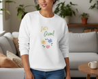 Person wearing a white sweatshirt with 'Let's Grow!' text and floral designs in a living room.