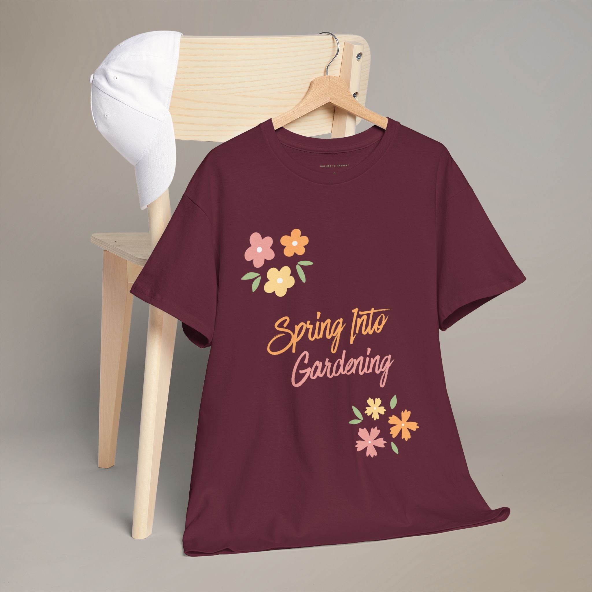 Maroon t-shirt with 'Spring Into Gardening' text and flowers on a hanger against a neutral background