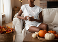 Woman sitting on a couch holding a mug with text, surrounded by pumpkins and fall decorations.