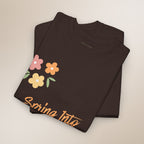 Folded black t-shirt with floral design and 'Spring Into' text on a beige background