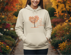Person wearing a beige hoodie with a tree design and text in an autumn garden.