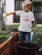 Child watering plants in a garden wearing a shirt with gardening text and images.