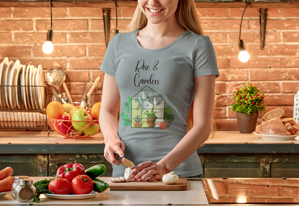 Woman in a kitchen wearing a t-shirt with a garden design, standing by a cutting board with vegetables.