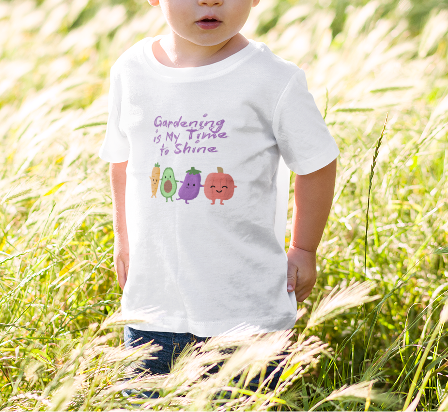 Child wearing a white t-shirt with colorful vegetables and text in a grassy field