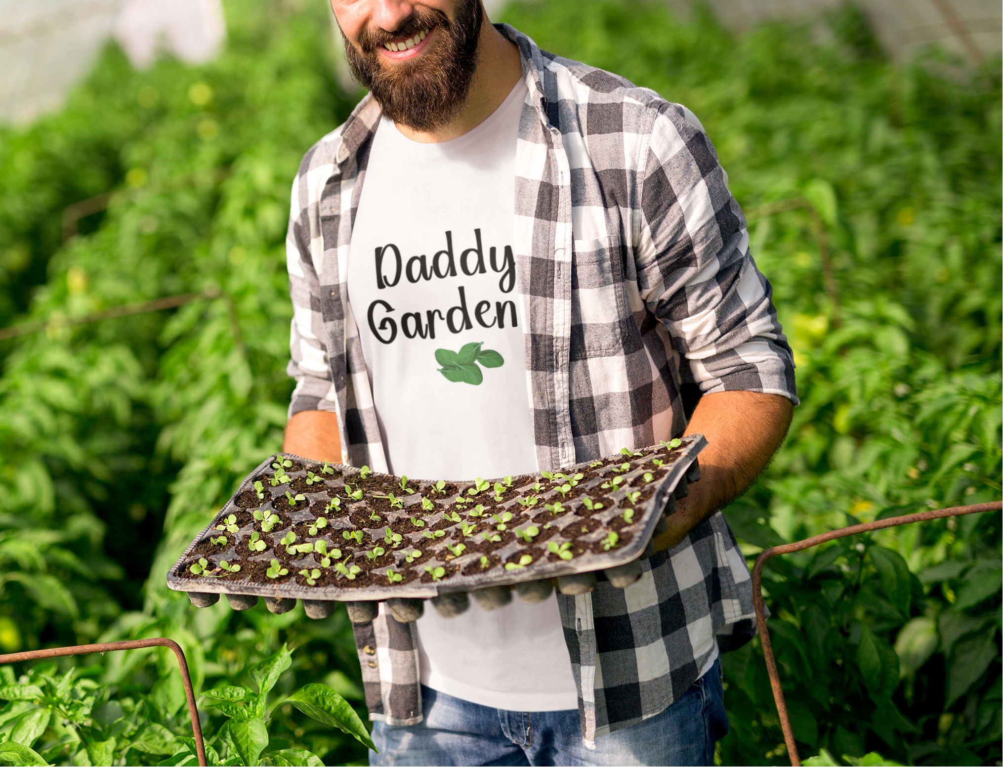 Man holding a tray of plants in a greenhouse with 'Daddy Garden' shirt