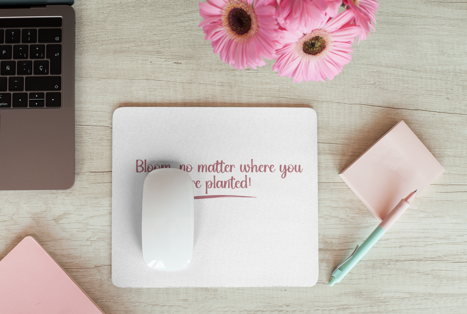 Laptop, mouse, pink flowers, and a pen on a wooden surface