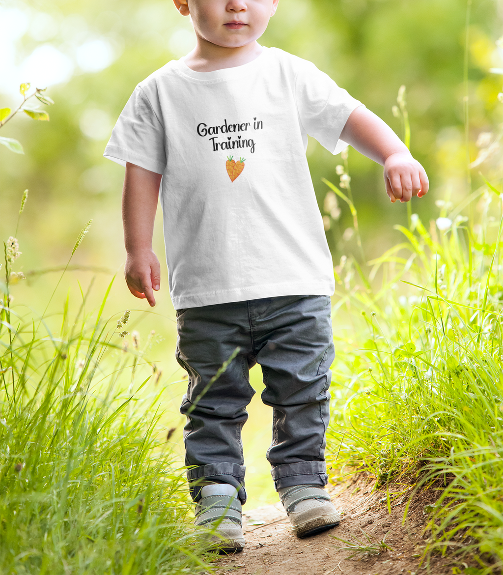 Child wearing a 'Gardener in Training' shirt walking on a path in a garden.