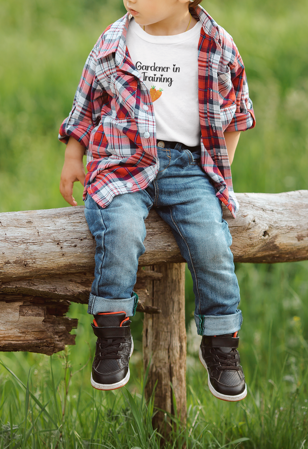 Child sitting on a log in a grassy field wearing a plaid shirt, jeans, and sneakers.