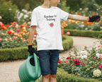 Child in a 'Gardener in Training' shirt with a watering can near an apple tree.