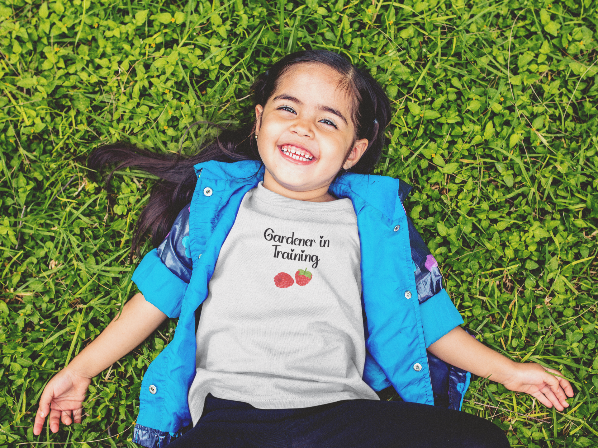 Child wearing a 'Gardener in Training' shirt lying on grass