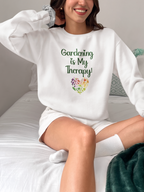 Person wearing a white sweatshirt with 'Gardening is My Therapy!' text and flower graphic.