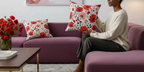 Woman sitting on a purple couch holding a floral pillow in a living room.