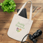 Beige tote bag with 'Daddy Gardener' text and plant design, surrounded by stationery items on a white background.
