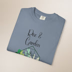 Folded blue t-shirt with 'Rise & Garden' text and terrarium design on a beige background