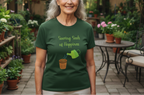 Woman wearing a green t-shirt with a graphic and text, standing in a garden setting.