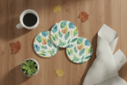 Set of four leaf-patterned coasters on a wooden surface with a cup of coffee and small plant.
