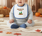 Baby wearing a bib with 'New to the Patch' text and pumpkin graphics, sitting on a blanket with pumpkins and leaves in the background.