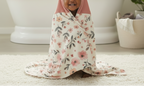 Child wrapped in a floral blanket on a light-colored floor.