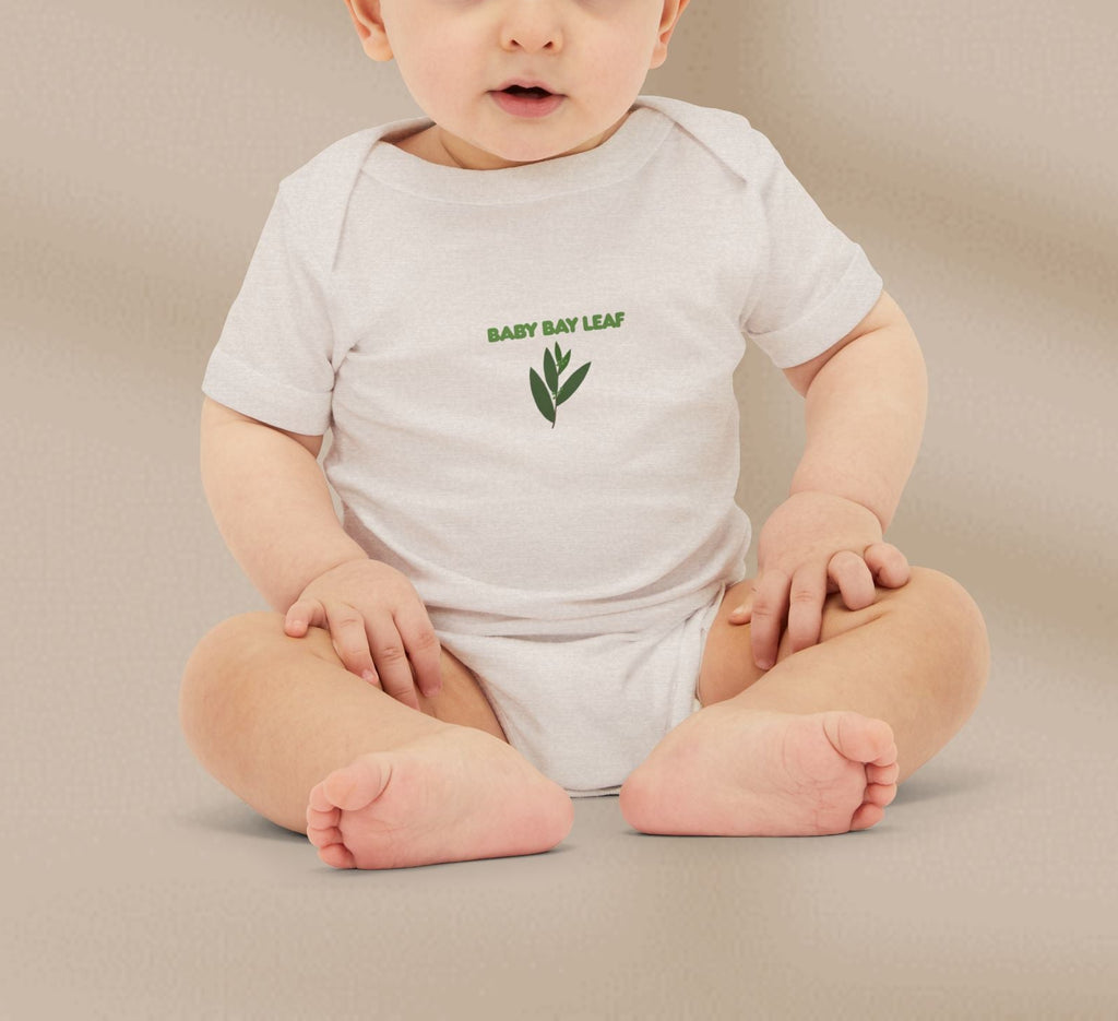 Baby wearing a white onesie with green text and leaf design on a beige background
