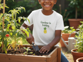 Child wearing a 'Gardener in Training' shirt with a pineapple graphic, planting in a garden.
