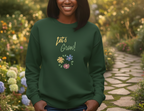 Person wearing a green sweatshirt with 'Let's Grow!' text and floral designs in a garden setting
