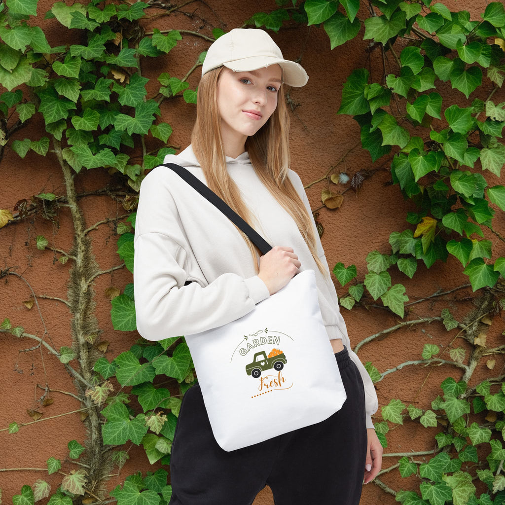Woman holding a white tote bag with a design against a wall with green ivy