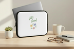 Laptop with a white sleeve featuring 'Let's Grow!' text and floral design on a desk with a cup, glasses, and notebook.