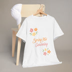 White t-shirt with 'Spring Into Gardening' text and flowers on a wooden chair.